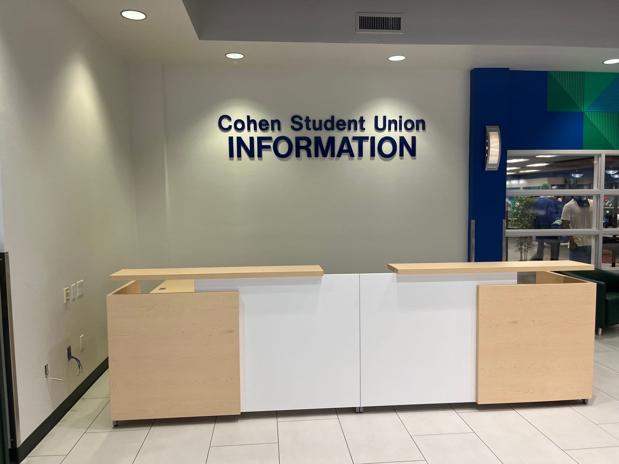 Cohen Student Union information desk in maple and white laminate beneath blue dimensional lettering